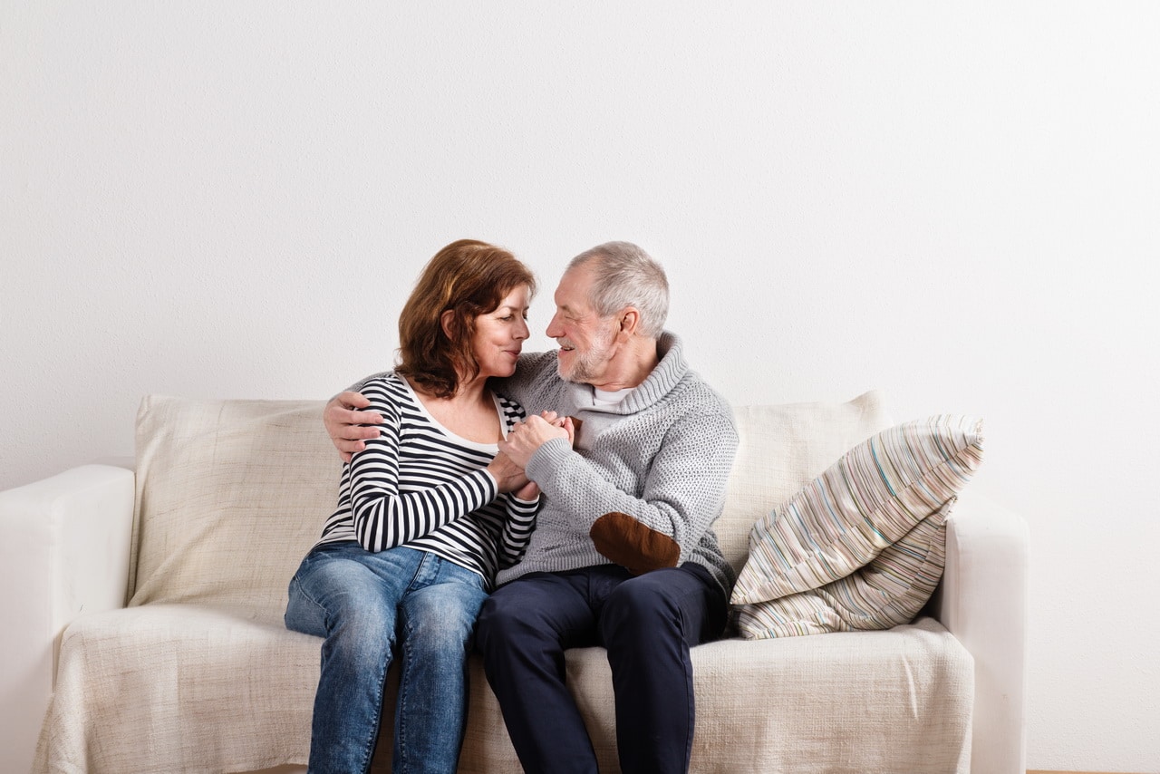 Beautiful Senior Couple Sitting On Couch, Hugging. Studio Shot.