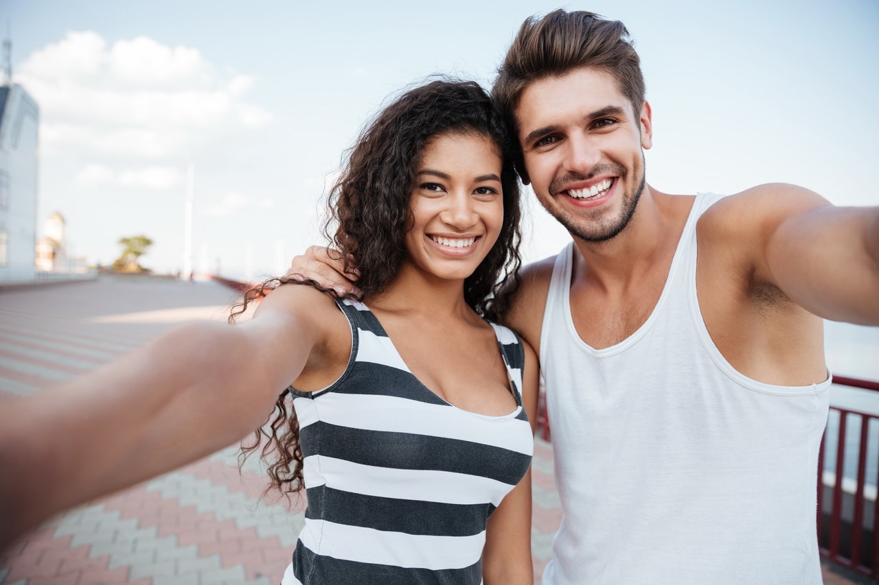 Happy Couple Standing And Taking Selfie Outdoors