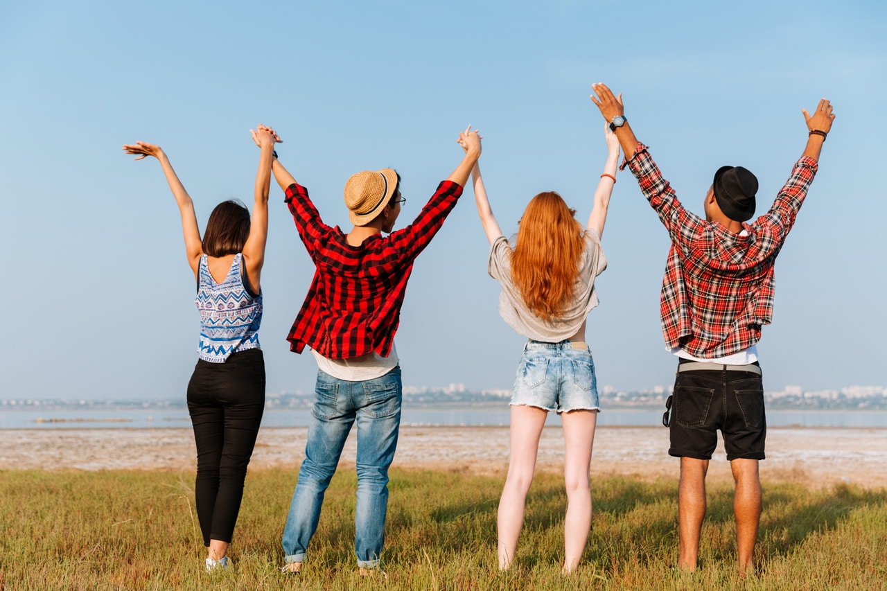 Back View Of Friends Standing And Holding Raised Hands Outdoors